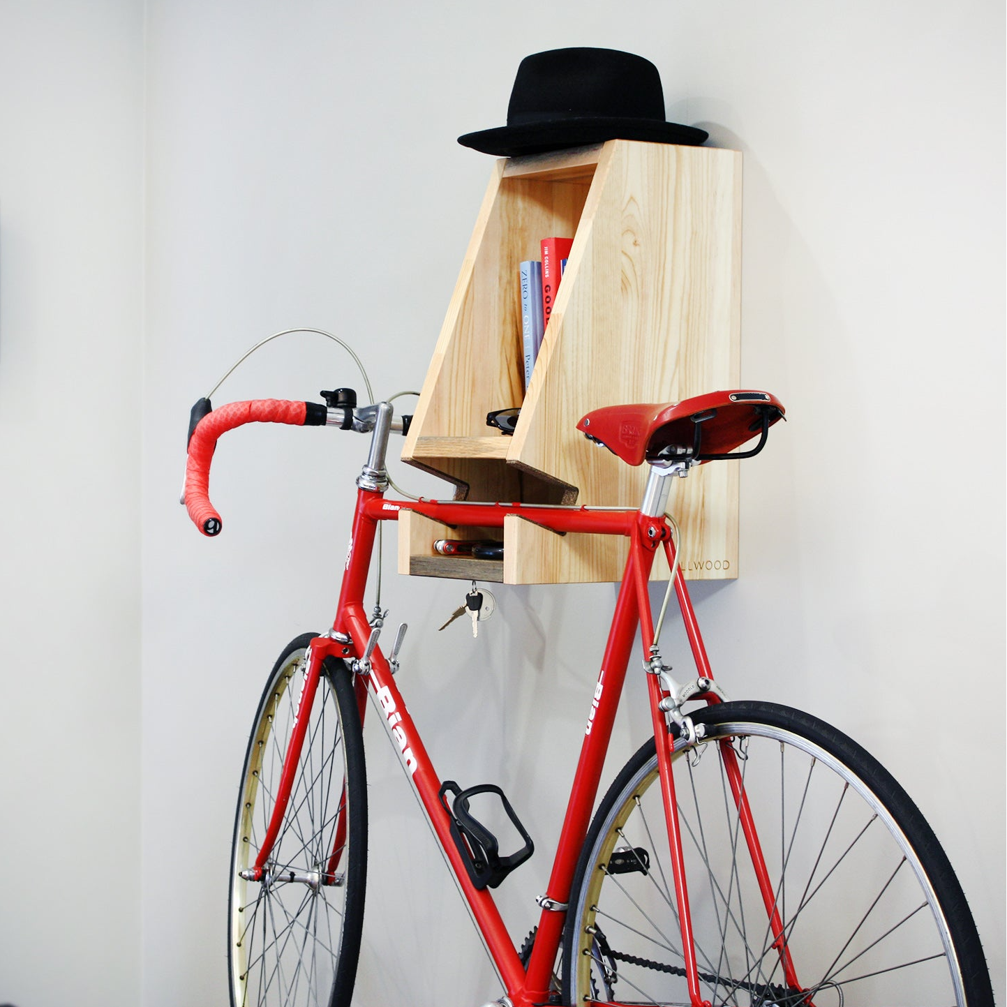 Red bicycle with a wooden shelf attached to the wall, holding books and a black hat.