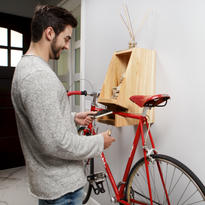 Man adjusting a red bicycle with a wooden bike rack attached to the wall.